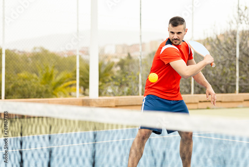 An adult man in sportswear is playing a game of pickleball on an outdoor court.The man is making a backhand with the racket to hit the ball.Pickle ball concept. Men Playing Pickleball