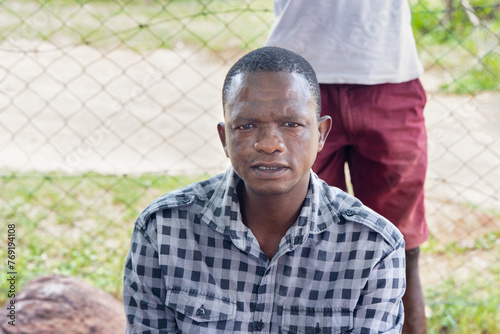 portrait of african man villager siting in the yard in front of a mesh fence outdoors , village life