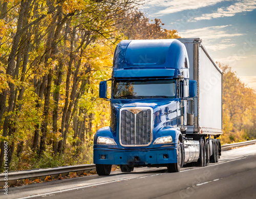 Bonnet blue big rig semi truck tractor carry cargo semi trailer driving on the autumn highway road with forest on the side