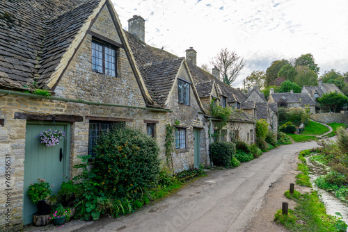 Scenic view of traditional old cottage houses and a street by a river in a beautiful English village, Bibury village in the Cotswolds Area of Outstanding Natural Beauty in Cirencester, England.