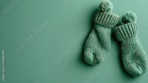 A pair of cozy knitted socks with pom-poms on a green background.