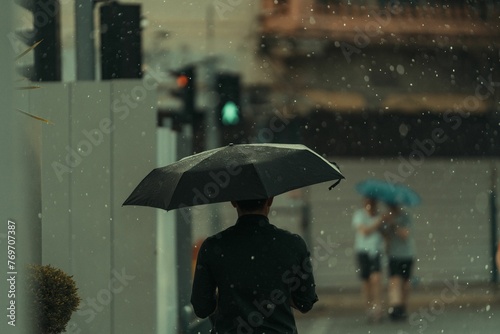 Person is walking alone in the rain, protected from the elements by a black umbrella