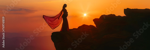 an indian mother drapped in a saree carrying her pregnancy standing on top of a cliff mountain silhouette shot sunset evening