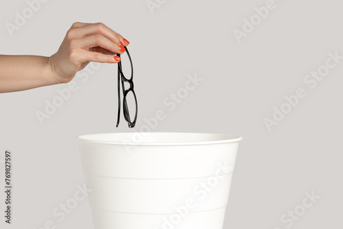 Closeup of woman hand trowing away glasses after eyesight treatment. Indoor studio shot isolated on gray background.