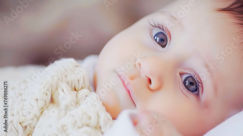 Close-up of a baby with striking blue eyes, warmly wrapped and looking pensive. 