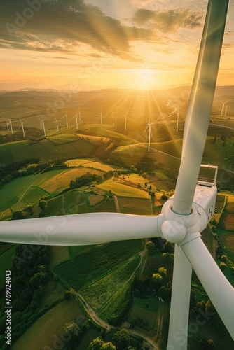 View from the top of a wind turbine overlooking a green fields and other wind turbines. A panoramic view of wind energy as turbines dot the landscape against a backdrop of green fields.