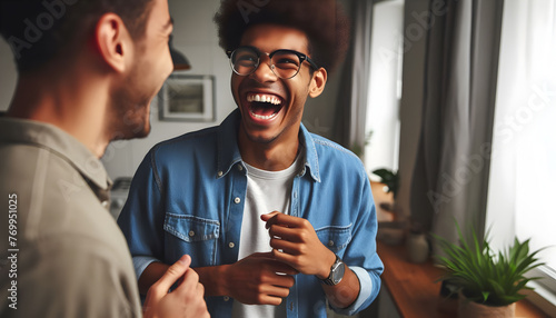 an overjoyed biracial young man in glasses, standing and laughing while engaged in a lively conversation with a friend or colleague. He’s a happy,