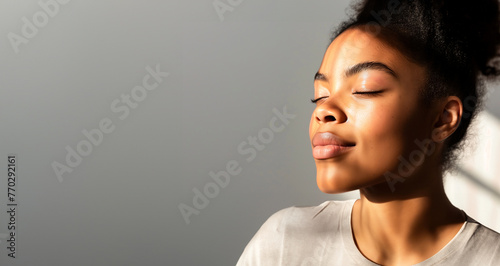 A beautiful african woman with closed eyes is enjoying the sunlight on her face, copy space for text banner on grey background