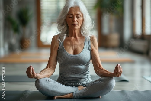 Tranquil senior woman meditating in yoga pose with eyes closed in a serene indoor environment