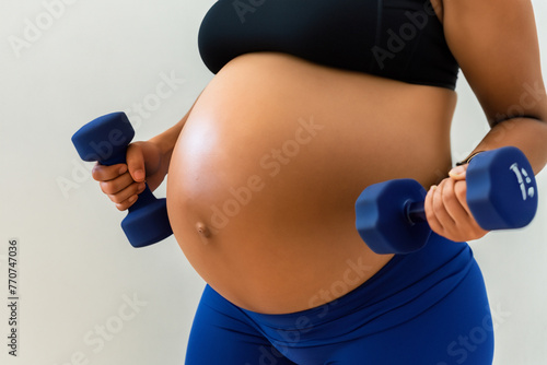 girl with dumbbells. pregnant girl in a black top holds blue dumbbells in her hands, sports concept