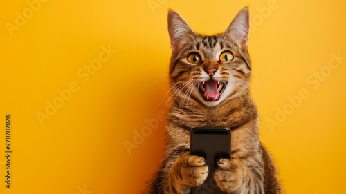 domestic cat holding a cell phone with its paws on a plain yellow background simulating a studio photo