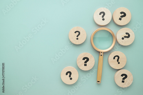 Magnifying glass with many question marks round wood blocks, find the answer among many choices, research, and decision concept