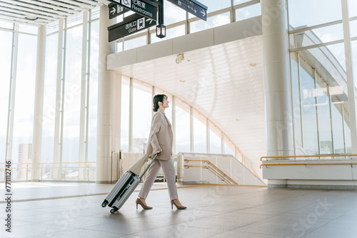 空港・駅・ビル・公共交通施設でスーツケースを持って歩くビジネスウーマン（海外出張・徒歩） 