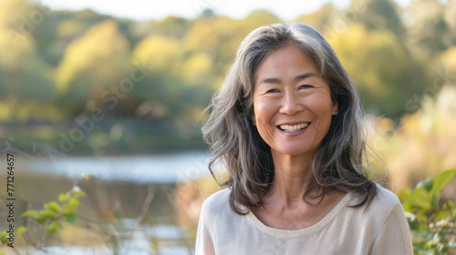 Asian american woman in her 50s who exudes happiness and a sense of feeling truly alive in a beautiful natural park near a lake, genuine smile on her face, relaxed and confident, female who found joy