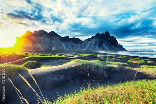 Dramatic sunny day and gorgeous rippled black sand beach and green grass on Stokksnes cape in Iceland.