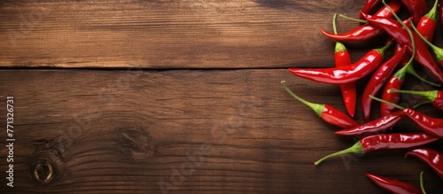 A close-up view of a variety of red hot peppers arranged on a rustic wooden table in natural light