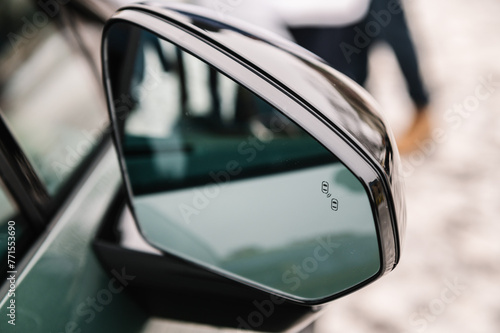 Blind zone monitoring sensor on the side right mirror of a new modern electric sedan car. View of the side mirror shows the light of blind spot to notice driver beware before changing lanes. Closeup.