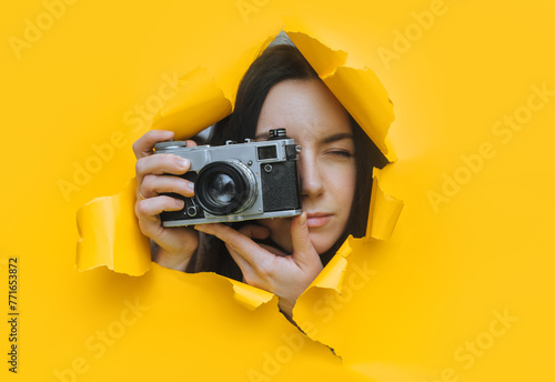 A young paparazzi girl with a rare SLR camera looks out from her hiding place and carefully watches what is happening. Yellow paper hole. Tabloid press. Looking for a subject for stock photos.