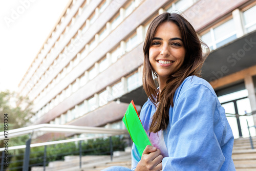 Young female college student sitting on stairs outside university building. Young woman looking at camera. Copy space.