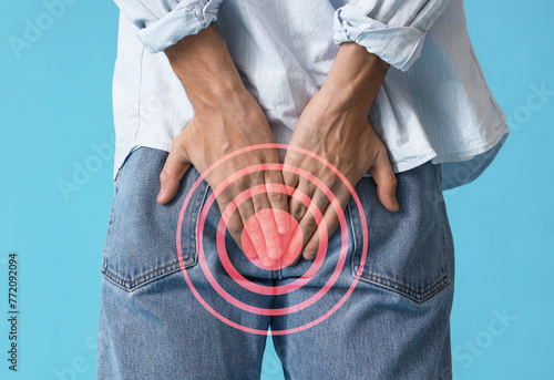 Young man with hemorrhoids on blue background, back view