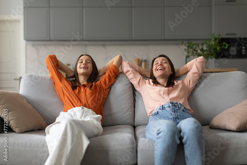 Calm mom and daughter relax on couch hands over head, lying on sofa resting with eyes closed, mother chilling with teenage girl
