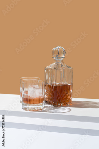 Vasos de whisky con hielo y decantador sobre fondo naranja 