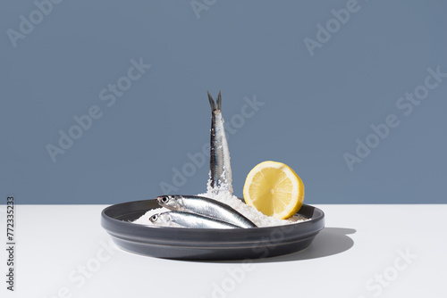 Tres anchoas frescas con medio limón sobre un plato lleno de sal sobre fondo azul 