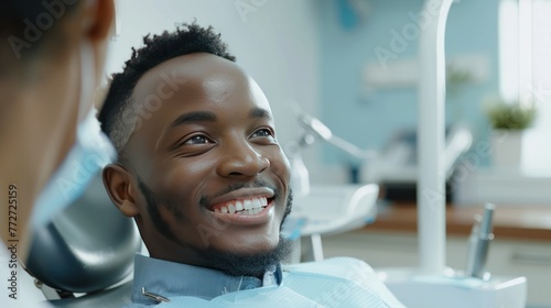 black dentist talking to male patient after oral cosmetic procedure, they both smile satisfied 