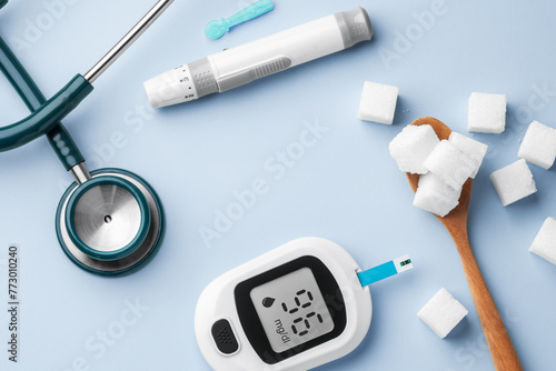 Blood glucose meter with stethoscope, lancet and sugar cubes in spoon on table, top view