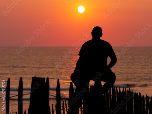surfer assis sur une barrière à contre-jour en attendant une vague devant la mer au coucher du soleil
