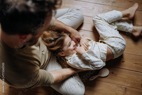 Top view of father with daughter on floor laughing together, having fun, tickling each other. Girls dad. Unconditional paternal love, Father's Day concept.