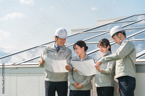 太陽光発電・ソーラーパネルの前に立つ電力会社・電気工事業者の作業着姿の技術者（クリーンエネルギー） 