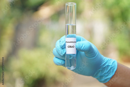 Close up hand wear blue glove, holds test tube of Formaldehyde liquid with molecular formula CH2O. Concept, chemical substance, colorless, toxic, strong-smell and flammable 