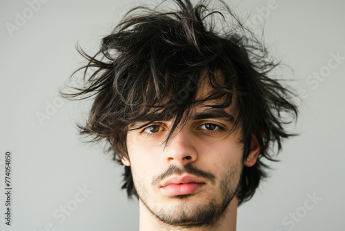 Trendy young adult man with a modern shaggy hairstyle and unkempt look in a close-up portrait, showcasing his stylish and individual fashion sense in a casual, natural, and contemporary way