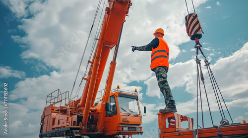 A construction worker in a high-visibility vest and hard hat is gesturing upwards, directing a crane at a construction site. 