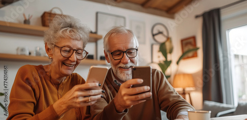 Happy older mature senior family couple, middle aged man and woman looking at cell phone using smartphone mobile technology device together and talking sitting at home table doing online shopping.