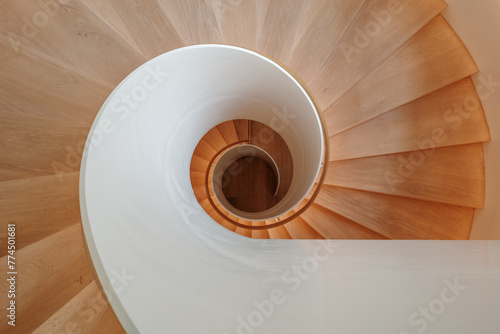 An overhead view of a contemporary spiral staircase with a flawless white balustrade and warm wooden steps that elegantly twist downwards, creating a mesmerizing architectural pattern.