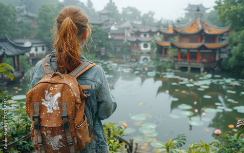 A woman with a backpack is standing by a pond in front of a row of buildings. The scene is peaceful and serene, with the woman taking in the beauty of the surroundings