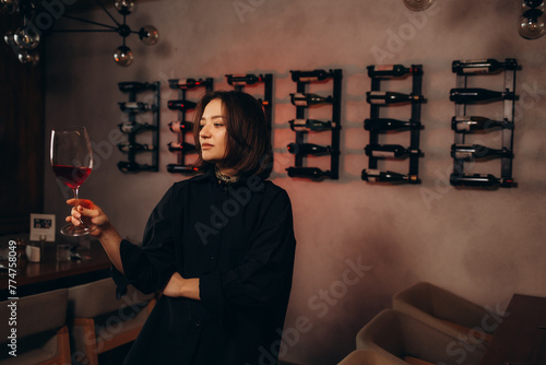 Woman in the wine cellar with barrels in background drinking and tasting wine.