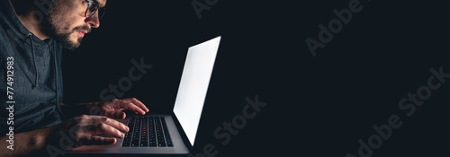 A man stares intently at a computer screen in the dark at night, copy space.
