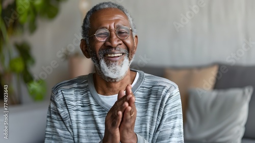 A happy senior man in living room clapping with joy and inspiration