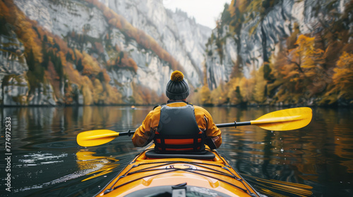 rear view of a man on a kayak floating on a serene mountain lake surrounded by steep cliffs and forest in autumn