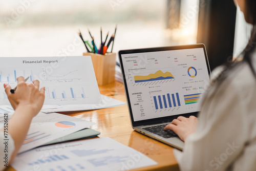 Two businesspeople or an accountant team are analyzing data charts, graphs, and a dashboard on a laptop screen in order to prepare a statistical report and discuss financial data in an office.