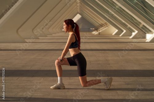 Athletic woman in sportswear stretching legs before doing workout outside in morning