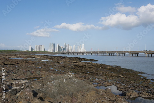 Wattenmeer an der Küste von Panama-Stadt bei Niedrigwasser am Meer mit Felsen und der als Hochstraße ausgeführten Umgehungsstraße Corredor Sur sowie die Skyline mit Hochhäusern im Hintergrund