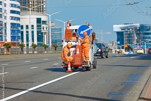 Minsk, Belarus. Apr 1, 2024. Workers in orange uniform on paint striping truck installing orange safety cones on freshly painted white stripes on asphalt road. Road marking work, renewal road marking