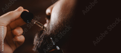 Barber applies for growth beard oil with dropper for man in barbershop. Concept spa cosmetic and treatment wellness and natural beauty of skin men
