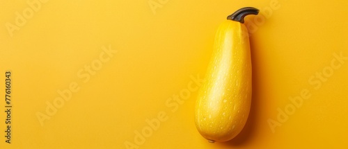  A solitary zucchini atop a yellow table, near a black food item on a similar yellow surface