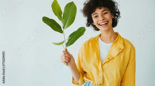 Linda mulher usando uma camiseta amarela e segurando um ramo de planta verde no fundo azul claro