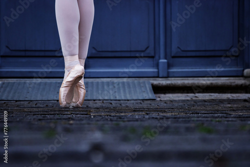 Closeup of a dancer legs balancing on the pointe shoes. Ballerina wearing ballet slippers while standing on her tips on the cobblestone road. Grey retro doors on the background. Selective focus